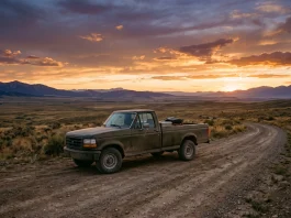 A pickup truck parked on a rural road under a vast sky at sunset.