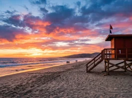 A red lifeguard tower on a beach at sunset.