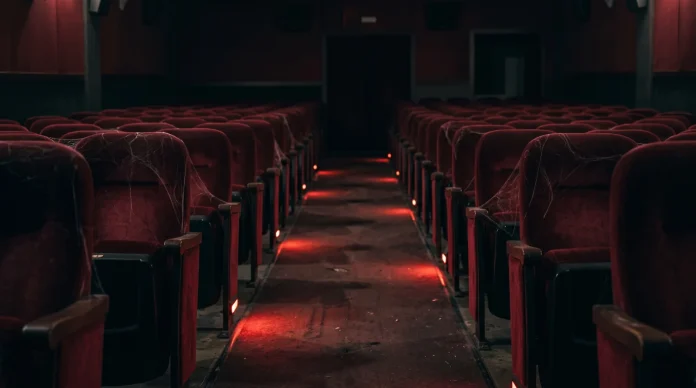 Conceptual image of an empty dark movie theater with red lighting and spider webs.