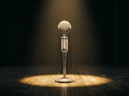 A silver vintage microphone under a spotlight on a dark stage.