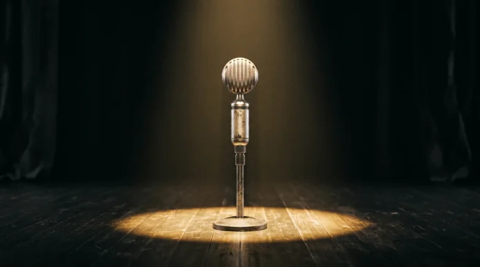 A silver vintage microphone under a spotlight on a dark stage.