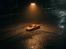 A miniature orange car on a dark asphalt road under a streetlamp.