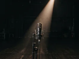 A professional microphone on a dark stage under a narrow spotlight.