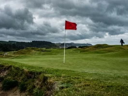 A solitary red golf flag on a green under a dramatic sky.