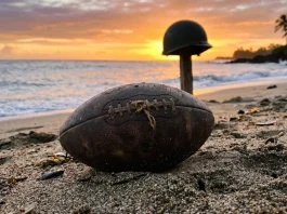 The Mosquito Bowl Review: Peter Berg’s Visceral WWII Football Drama A vintage leather football sitting in tropical sand with a military helmet in the background.