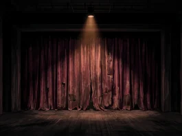 A lonely spotlight on a worn theater curtain in a dark room.