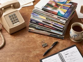 A conceptual photo of a 90s magazine office desk with stacks of periodicals and a tea mug.